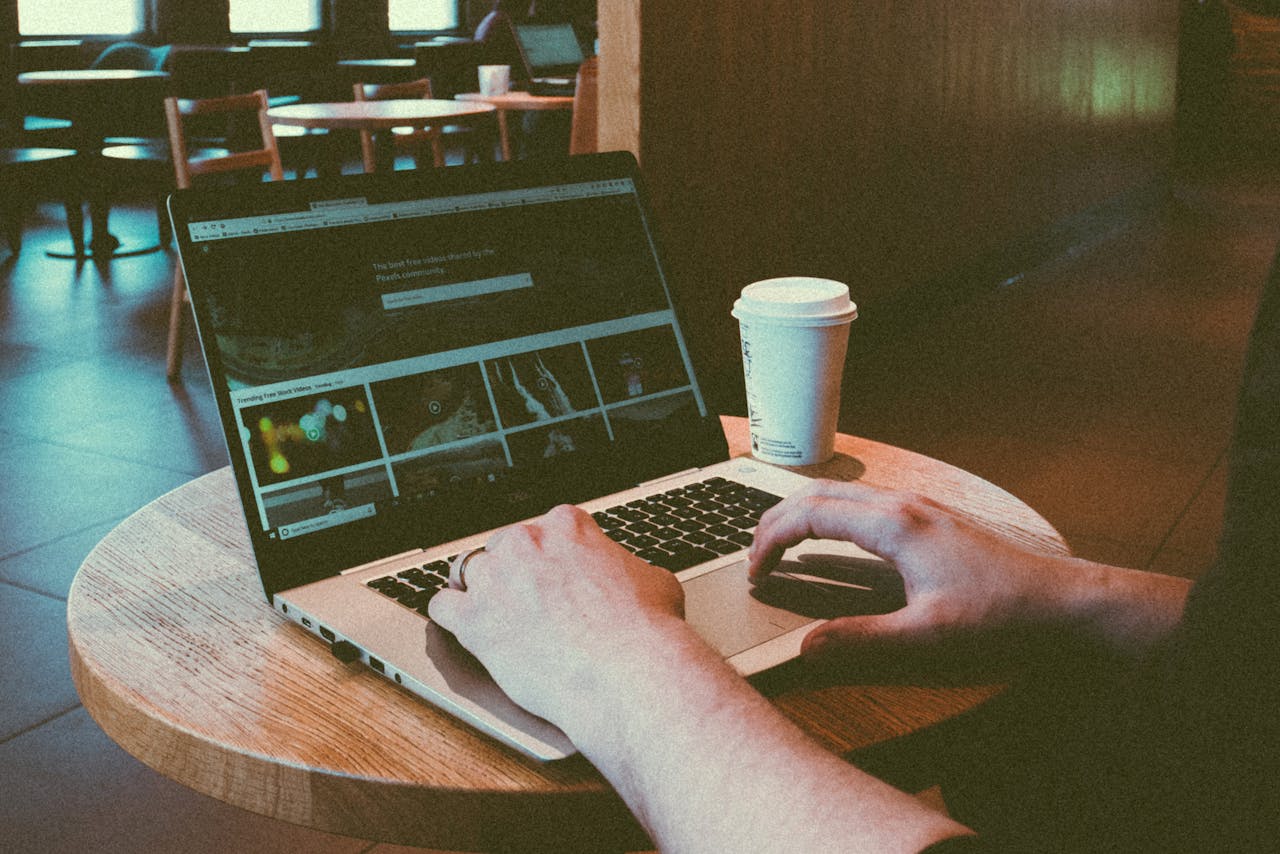 Usługi Person using a laptop in a cozy café, highlighting remote work lifestyle with a coffee cup on the table.